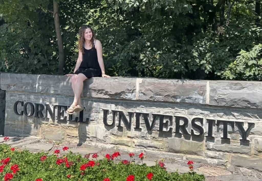 Boyce Thompson Institute entrance with young woman sitting on the stone sign, surrounded by lush greenery, representing a leading plant science research and education institution.