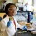 Young African American female scientist in laboratory holding fresh green plant sample at Boyce Thompson Institute, engaged in plant science research and sustainable agriculture.